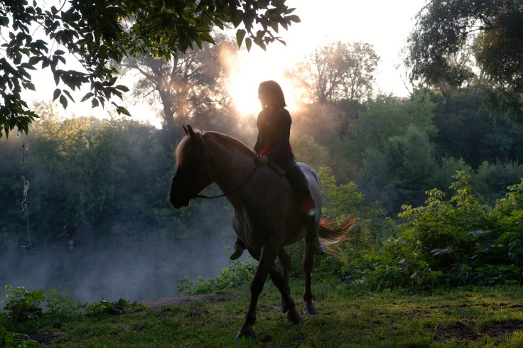Young woman riding a horse on a beautiful landscape. Clear lake at morning fog. Sunrise