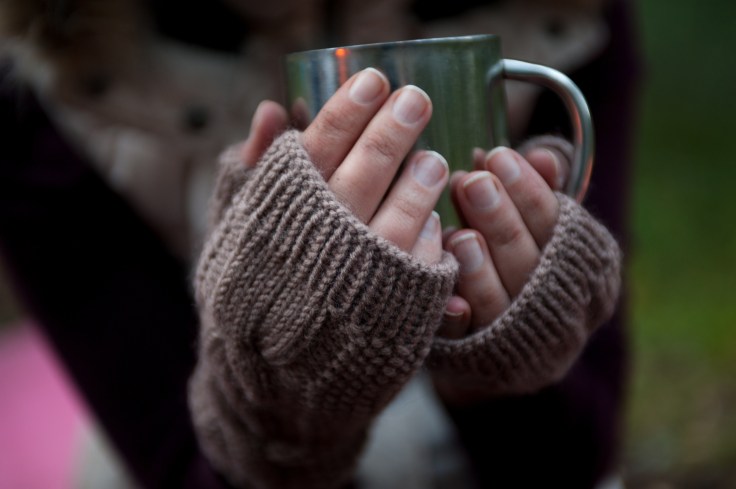 Metal mug with hot tea in a hands in a warm cozy mittens