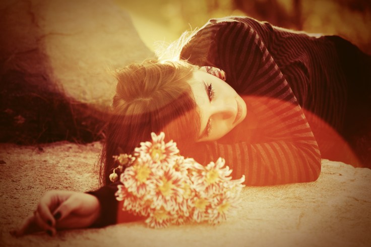 Sad young woman with a flowers lying on tombstone